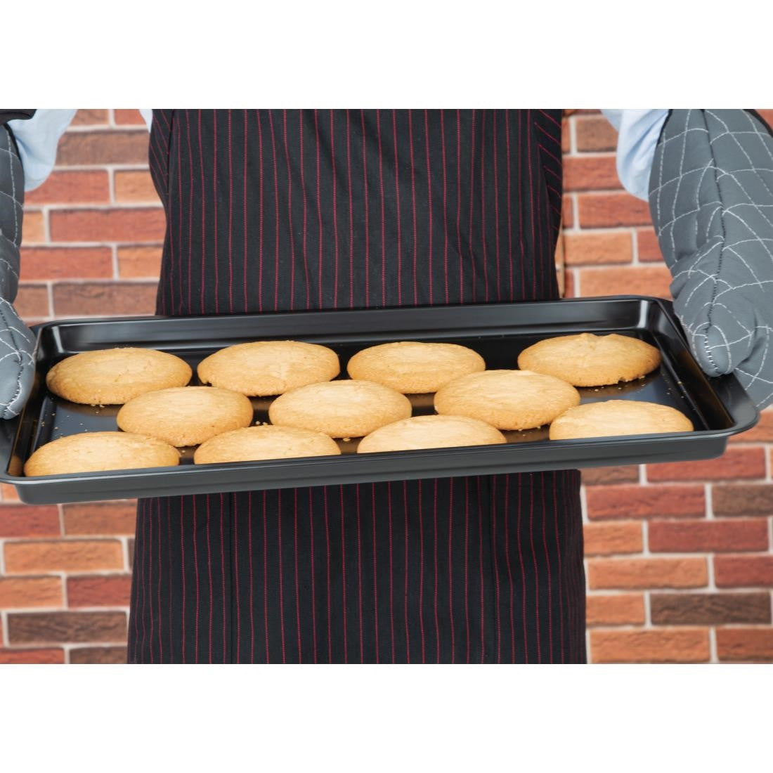 Chef holding Vogue Non-Stick Carbon Steel Baking Tray 482 x 305mm with baked cookies.