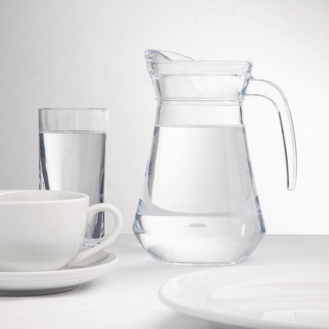Olympia Glass Jugs 1Ltr with content, glass of water, cups and saucer, and plates on table.